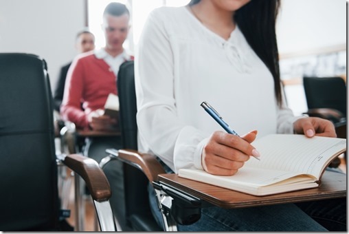 With notepad and pen in hands. Group of people at business conference in modern classroom at daytime.