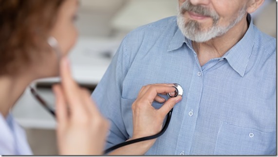 Close up young female general practitioner or cardiologist using stethoscope, checking heartbeat or listening lungs sounds of middle aged elder retired male patient at checkup appointment in hospital.