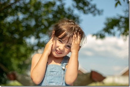 A little girl in a jeans sundress, two pigtails, juggles his hands behind his head and a sore ear
