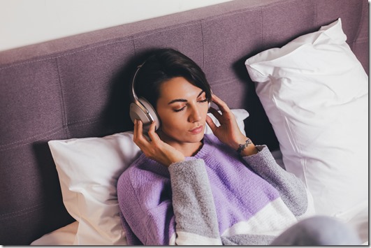 Happy woman at home on comfy bed wearing warm clothes pullover, listen music