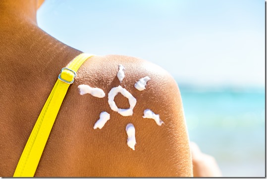 Back view of young woman tanning at the beach with sunscreen cream in sun shape on her shoulder, UV sunburn protection and sunblock skincare concept
