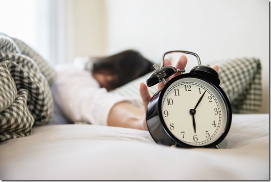 Sleepy woman reaching  holding the alarm clock in the morning with late wake up - every day life at home concept