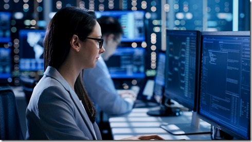 Female Engineer Controller Observes Working of the System. In the Background People Working and Monitors Show Various Information.