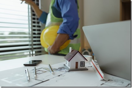 there are scientific calculator, laptop, house model, blueprint on the desk in the office with two architects, engineer is meeting with contractor about instruction project